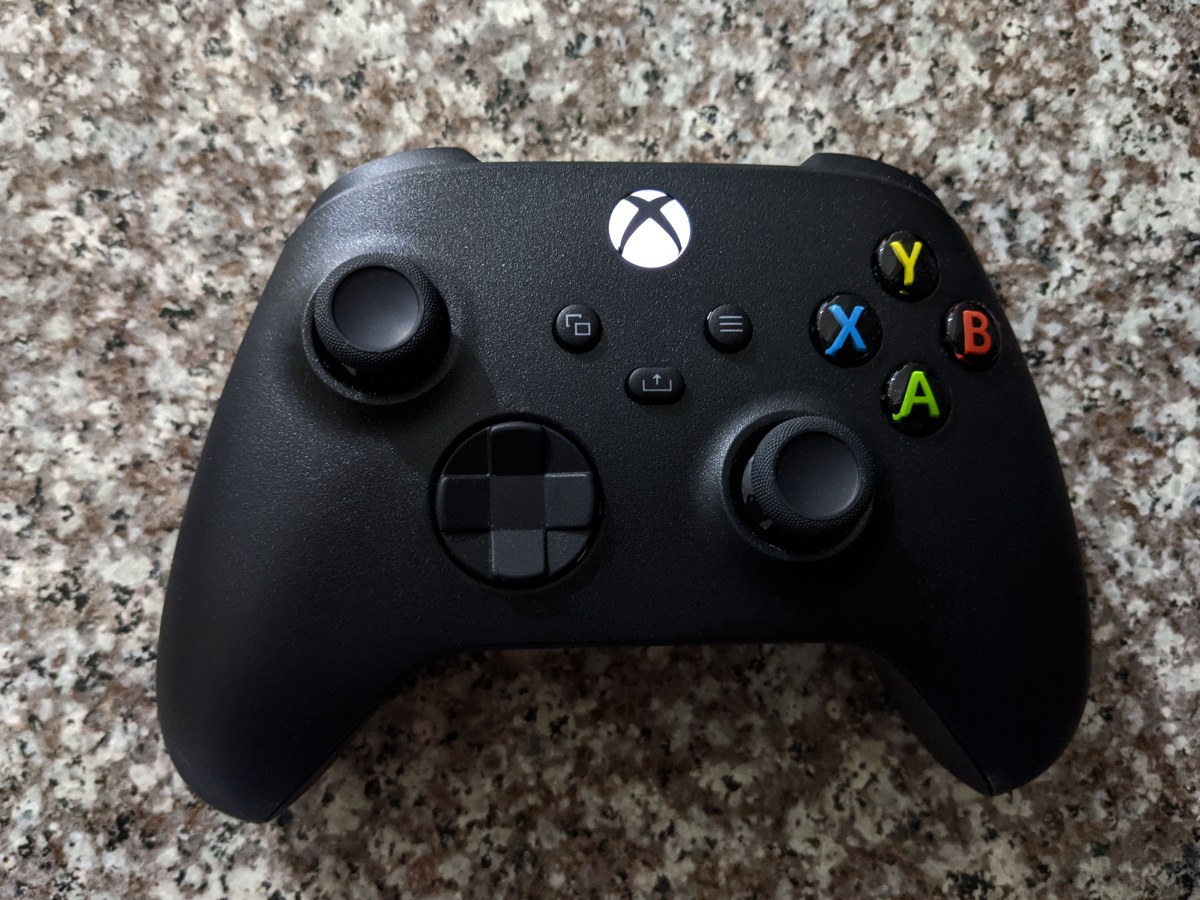 A real black Xbox Series controller resting on a speckled stone surface