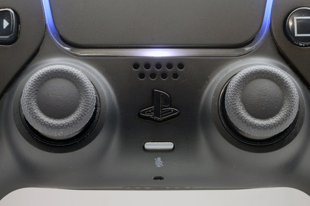Close-up of the two analogue sticks, speaker and PlayStation button on a black DualSense controller.