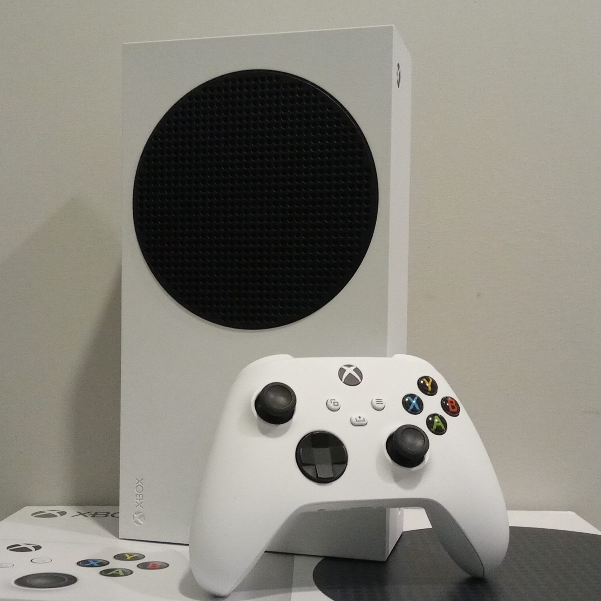 A white Xbox Series S standing on its retail box with a matching controller in front.