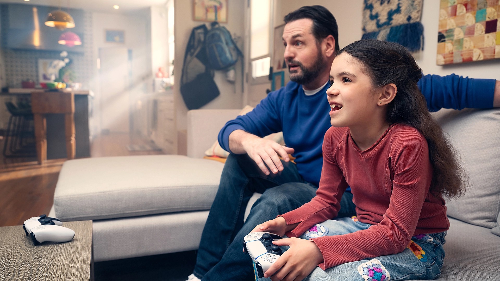 A parent and child playing together on a PS5 with DualSense controllers in a living room
